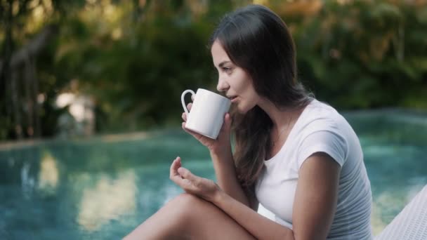 Vacker brunett dam dricker te från mugg vid poolen — Stockvideo