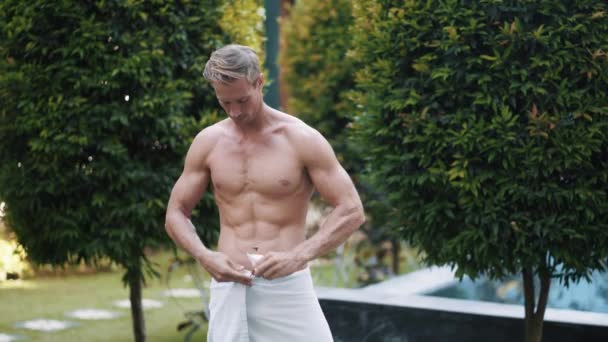 Man adjusts towel on waist near swimming pool in garden — Stockvideo