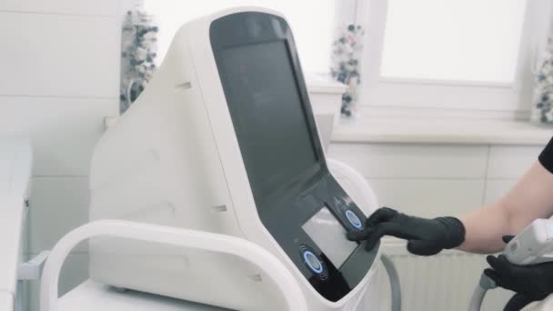 Zbliżenie rąk lekarza włącza sprzęt laserowy przed zabiegiem, widok z boku — Wideo stockowe