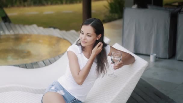 Beautiful girl with long hair holds glass sitting on couch — Stockvideo