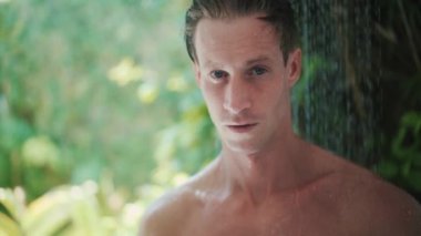 young man takes refreshing shower near green tropical plants