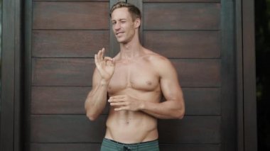 positive guy shows OK sign and winks at stylish wooden door
