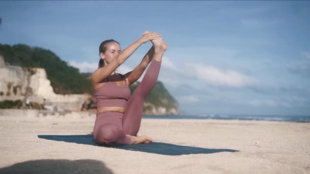 Menina em traje de treino estende a perna esquerda, fazendo ioga pose — Vídeo de Stock