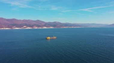 Kargo gemisi sakin mavi okyanus yüzeyinde dağlar boyunca yol alır.