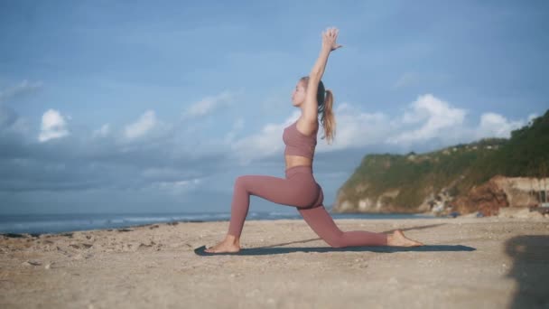 Eşofmanlı güzel bir kadın kumsalda yoga pozu veriyor. — Stok video