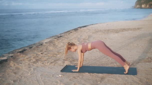 Chica en traje deportivo cómodo se extiende haciendo yoga en la playa — Vídeo de stock