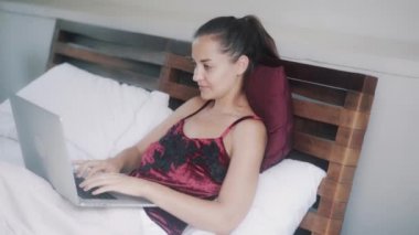 Güzel, neşeli kız laptopta çalışıyor. Yatakta portakal suyu içiyor.