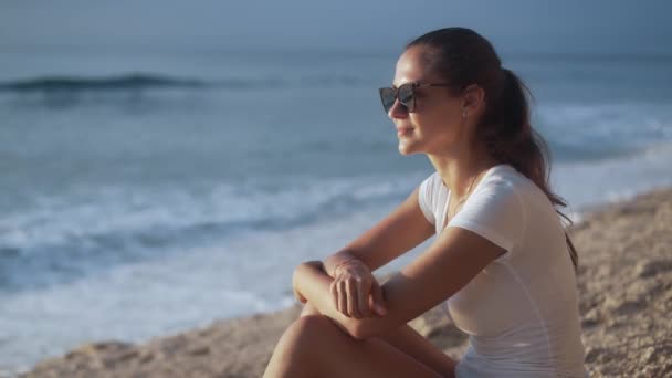 Portret pięknej uśmiechniętej kobiety w okularach przeciwsłonecznych patrzącej na morze o zachodzie słońca. — Wideo stockowe