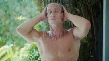 young man takes refreshing shower near green tropical plants
