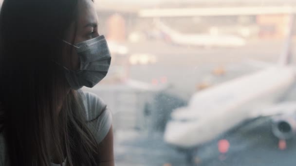 Вид сбоку, портрет женщины в защитной маске смотрит в окно аэропорта COVID-19 — стоковое видео