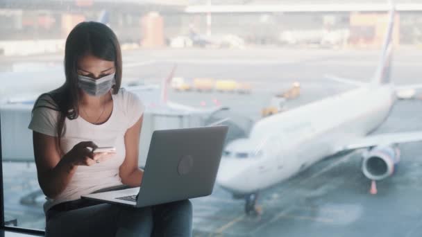 Mulher em máscara médica protetora usa laptop e smartphone no aeroporto, COVID-19 — Vídeo de Stock