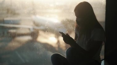 Koruyucu maskeli kadın silueti havaalanı COVID-19 'da akıllı telefon kullanıyor.