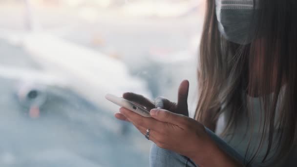 Mujer con máscara protectora utiliza smartphone, envía un mensaje en el aeropuerto COVID-19 — Vídeo de stock