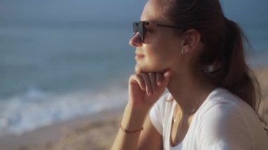 Güneş gözlüklü güzel bir kadın okyanus kıyısında gün batımını ve gökyüzünü izliyor..