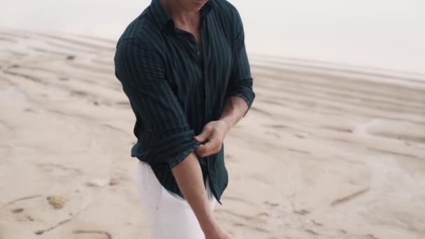 Samotny mężczyzna w czarnej koszuli spaceruje wzdłuż piaszczystej plaży. — Wideo stockowe