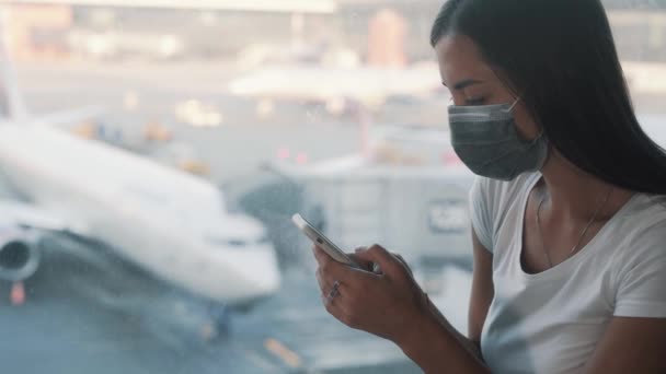 保護マスクの女性は、スマートフォンを使用して、空港でメッセージを送信COVID-19 — ストック動画