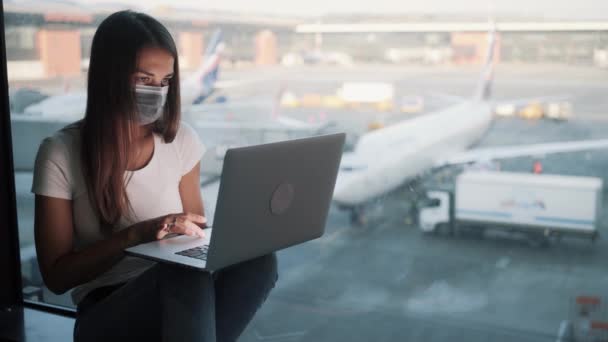 Женщина в защитной медицинской маске использует ноутбук для работы в аэропорту, COVID-19 — стоковое видео