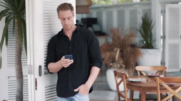 Hombre guapo en la camisa se pone en contra de la cafetería con estilo y utiliza el teléfono, enviar mensaje — Vídeos de Stock