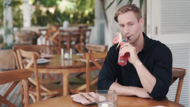 Hombre guapo bebiendo jugo de sandía en un elegante café, mira a la cámara, sonríe — Vídeos de Stock