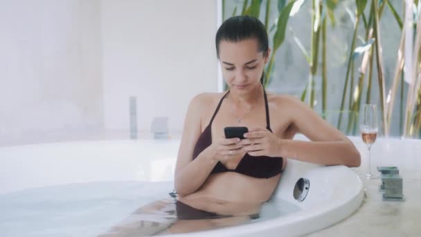 Jeune femme utilise smartphone assis dans une baignoire ronde moderne dans des appartements de luxe — Video