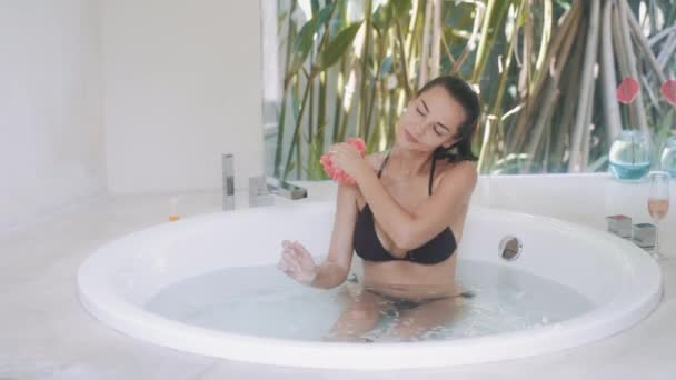 Attractive young woman in bikini washes body and taking bath in round bathtub — Stock Video