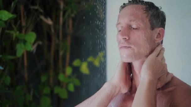 Портрет человека, принимающего душ в современной открытой ванной, зелени на заднем плане — стоковое видео