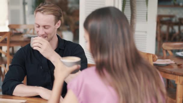 Pareja joven tomando café en la cafetería, chico y chica hablando y riendo — Vídeo de stock