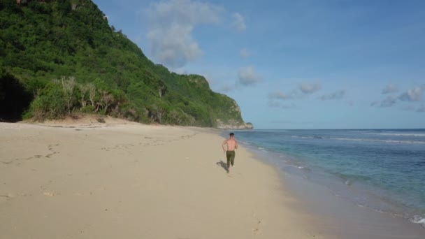 Sportler läuft allein am Sandstrand, im Hintergrund Meer und Berge — Stockvideo
