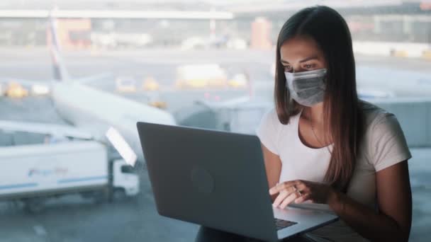 Menina em máscara médica protetora usa laptop para o trabalho no aeroporto, COVID-19 — Vídeo de Stock