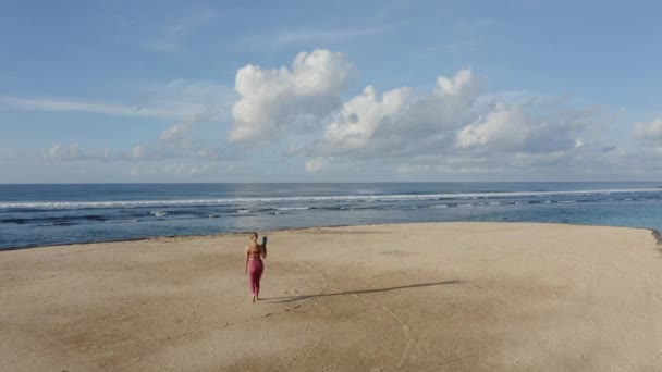 Flygfoto, ung kvinna i sportkläder med gymnastikmatta går till stranden — Stockvideo