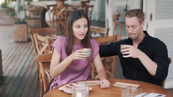 Pareja joven tomando café en la cafetería, chico y chica hablando y riendo — Vídeos de Stock