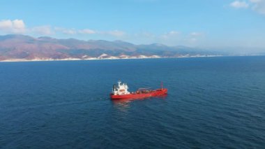 Deniz limanında yüzen kırmızı renkli kargo gemisinin havadan görünüşü, arka planda dağ