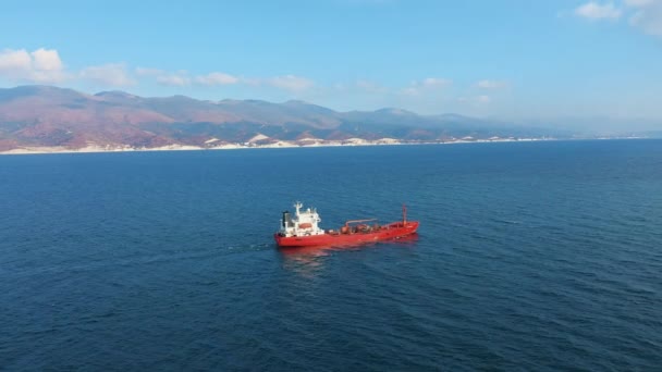 Widok z lotu ptaka na czerwony statek towarowy pływający w porcie morskim, góra na tle — Wideo stockowe