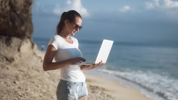 Струнка чарівна біла жінка в сонцезахисних окулярах працює з ноутбуком — стокове відео