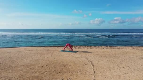 Drone footage Kobieta robi ćwiczenia jogi i rozciąga się na plaży z widokiem na ocean — Wideo stockowe