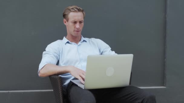 Man works with laptop, stretching arms, relaxing body, grey wall on background — Stock Video