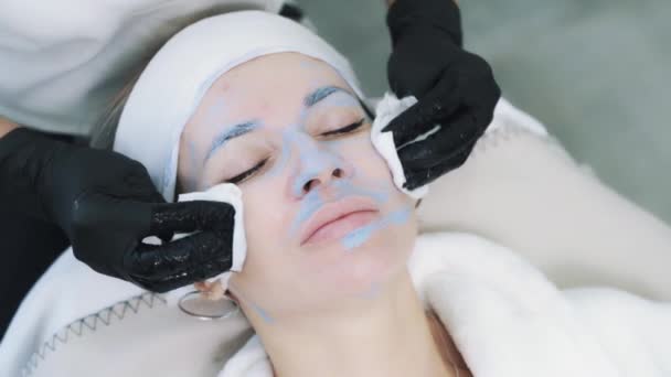 Top view of beautician removes blue clay mask from the skin of face — Stock Video