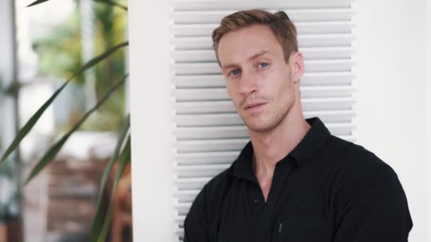 Portrait of blue-eyed handsome blond man in black shirt, looking at camera — Stock Video