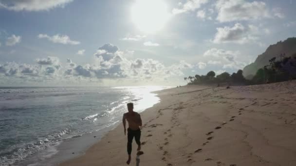Атлет с видом с воздуха бегает один по песчаному пляжу, океану и закату на заднем плане — стоковое видео
