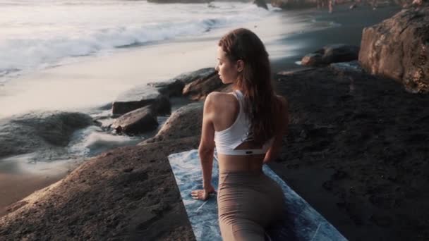 Fiatal nő csinál nyújtózkodik matrac fekete tengerparton, kilátással az óceánra és a hullámok — Stock videók
