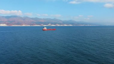 Deniz limanında yüzen kırmızı renkli kargo gemisinin havadan görünüşü, arka planda dağ
