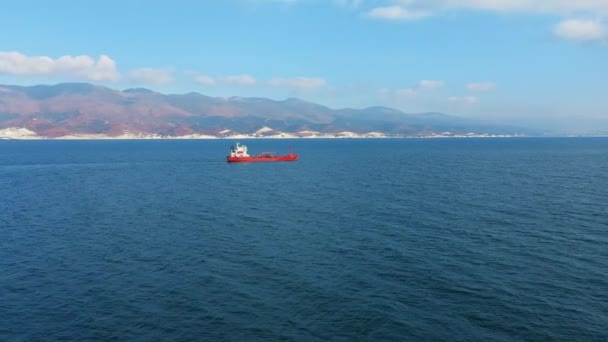 Вид с воздуха на плавучий в морском порту грузовой корабль красного цвета, горы на заднем плане — стоковое видео