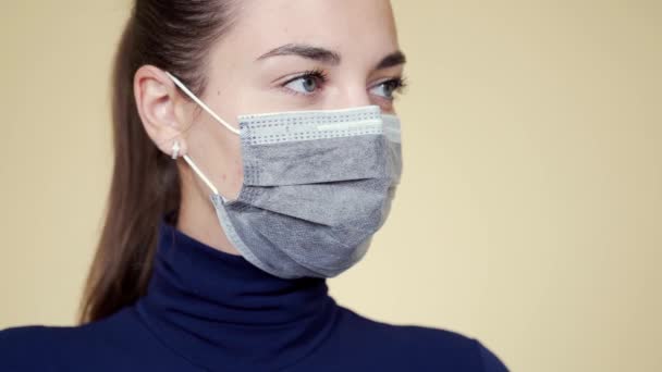 Retrato de mujer joven en máscara médica protectora mira hacia otro lado, cierra los ojos — Vídeos de Stock