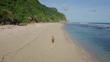 Hava manzaralı atlet kumlu sahilde, okyanusta ve arka planda dağlarda tek başına koşuyor.