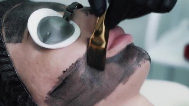 Genç ve güzel bir müşteriye karbon maske yapan bir güzellik uzmanının yakın çekimi.