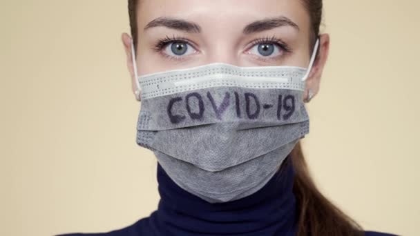 Portret van vrouw in beschermend masker met opschrift COVID-19 kijkend naar camera — Stockvideo