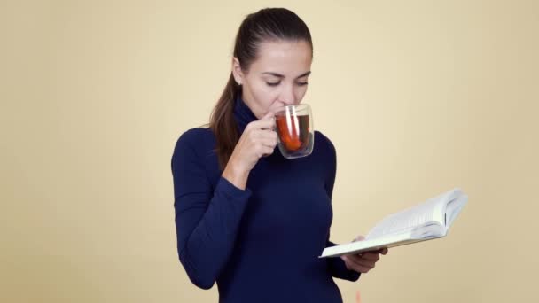 Kadın portresi sıcak çay içer ve bej arka planda izole edilmiş kitap okur. — Stok video