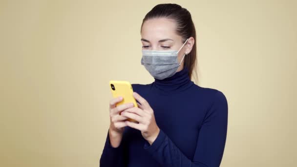 Retrato de mulher jovem em máscara médica usa telefone celular, fundo isolado — Vídeo de Stock