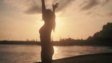 Sabahın erken saatlerinde güneşin altında yoga yapan bir kadın silueti.