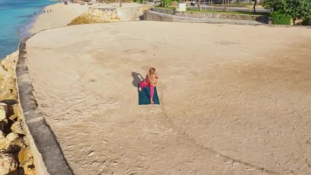 Женщина занимается йогой и растягивается на пляже с видом на океан — стоковое видео
